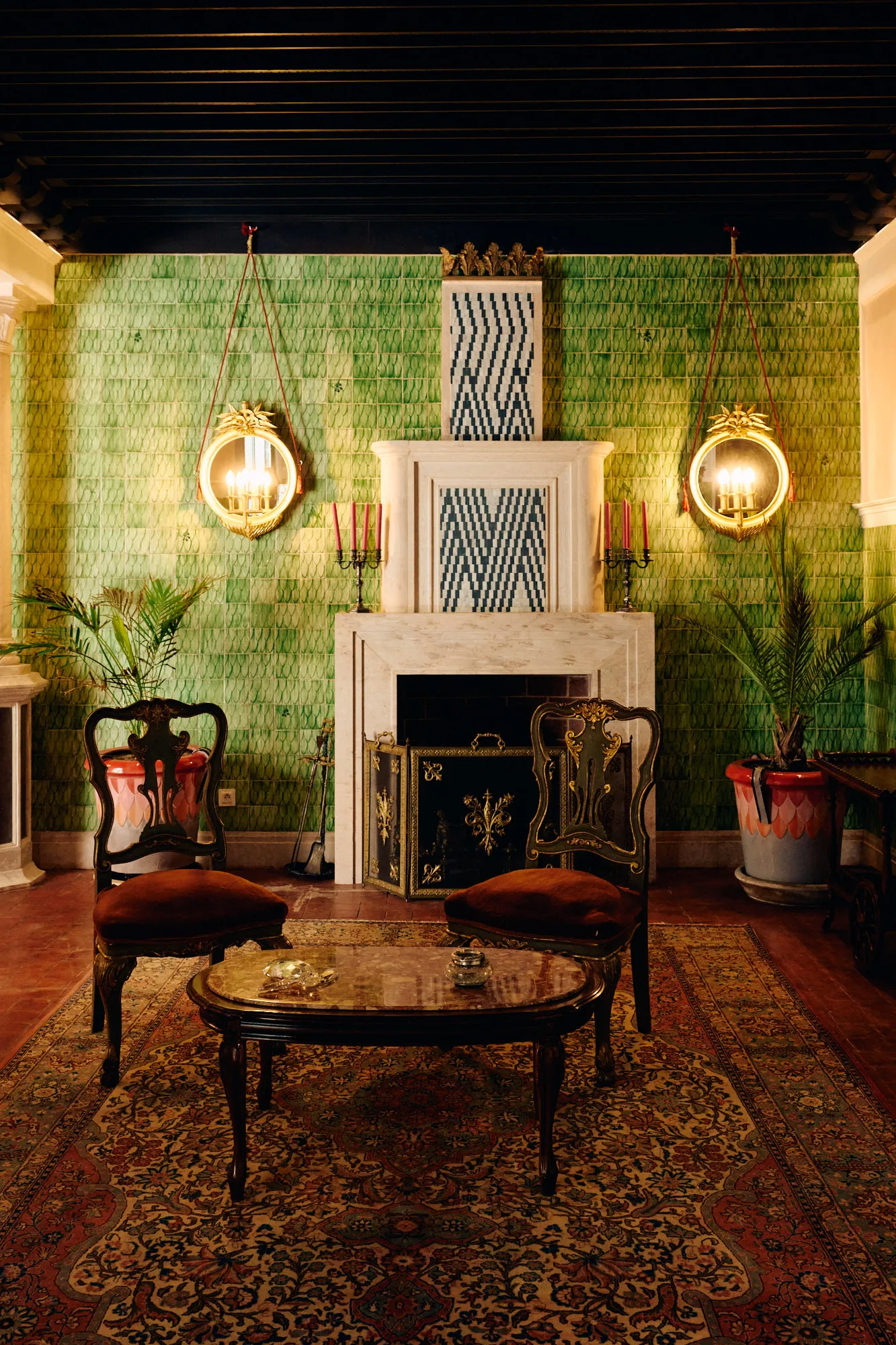 A green tiled salon with a marble fireplace and wall sconces.
