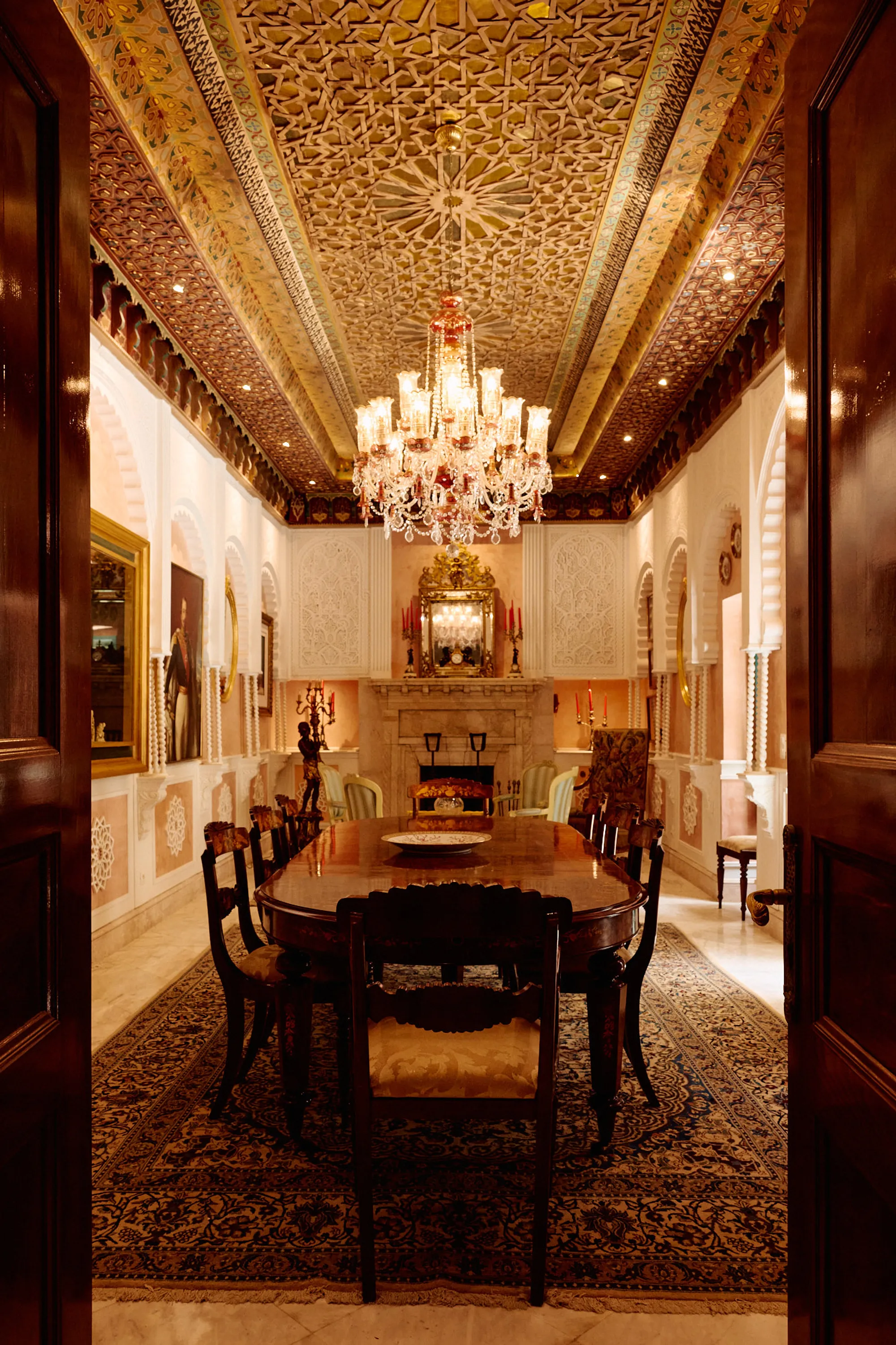 A dining room laid beneath its chandelier and painted ceiling.