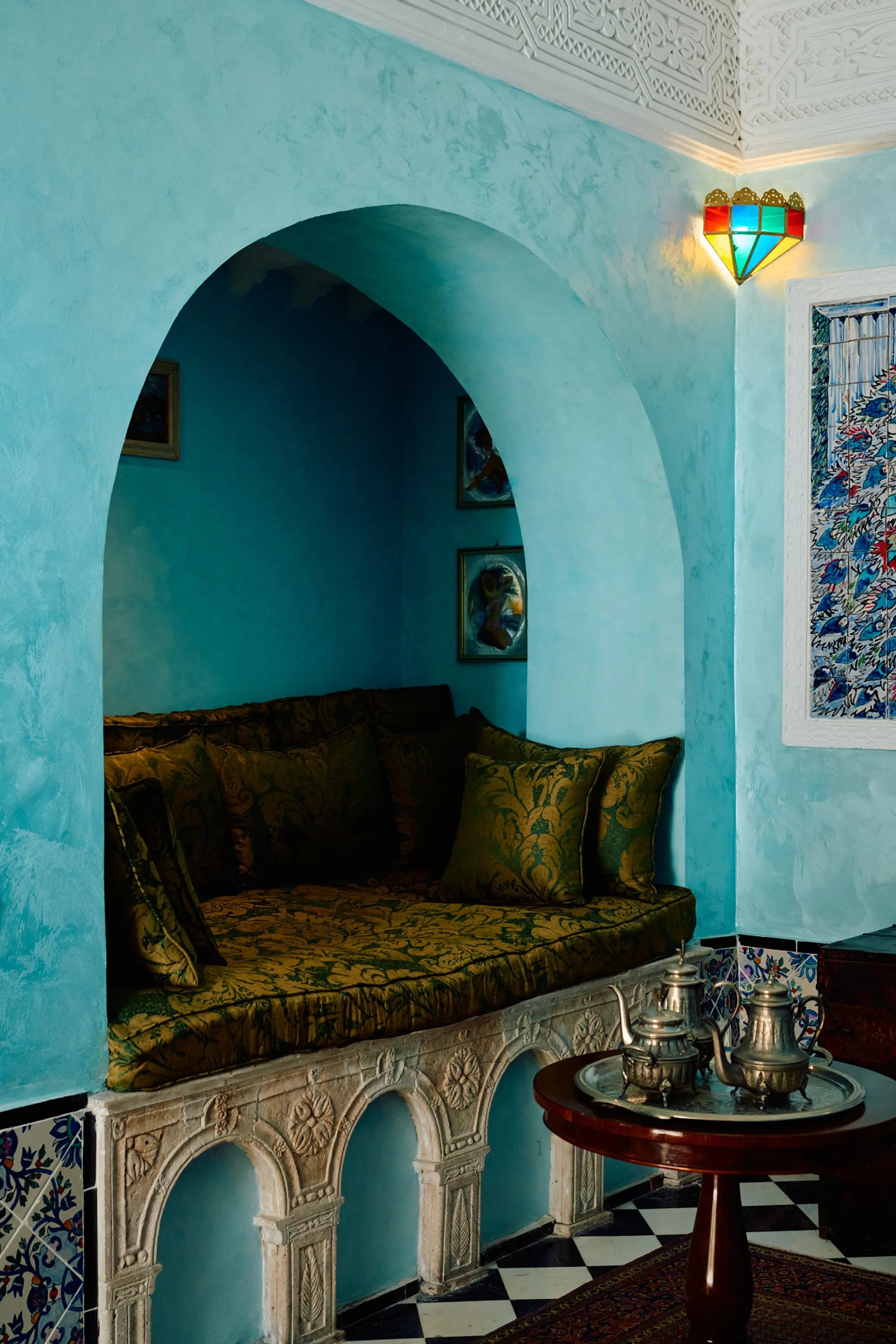 A turquoise room with a carved arch, a green banquette and a chequerboard floor.