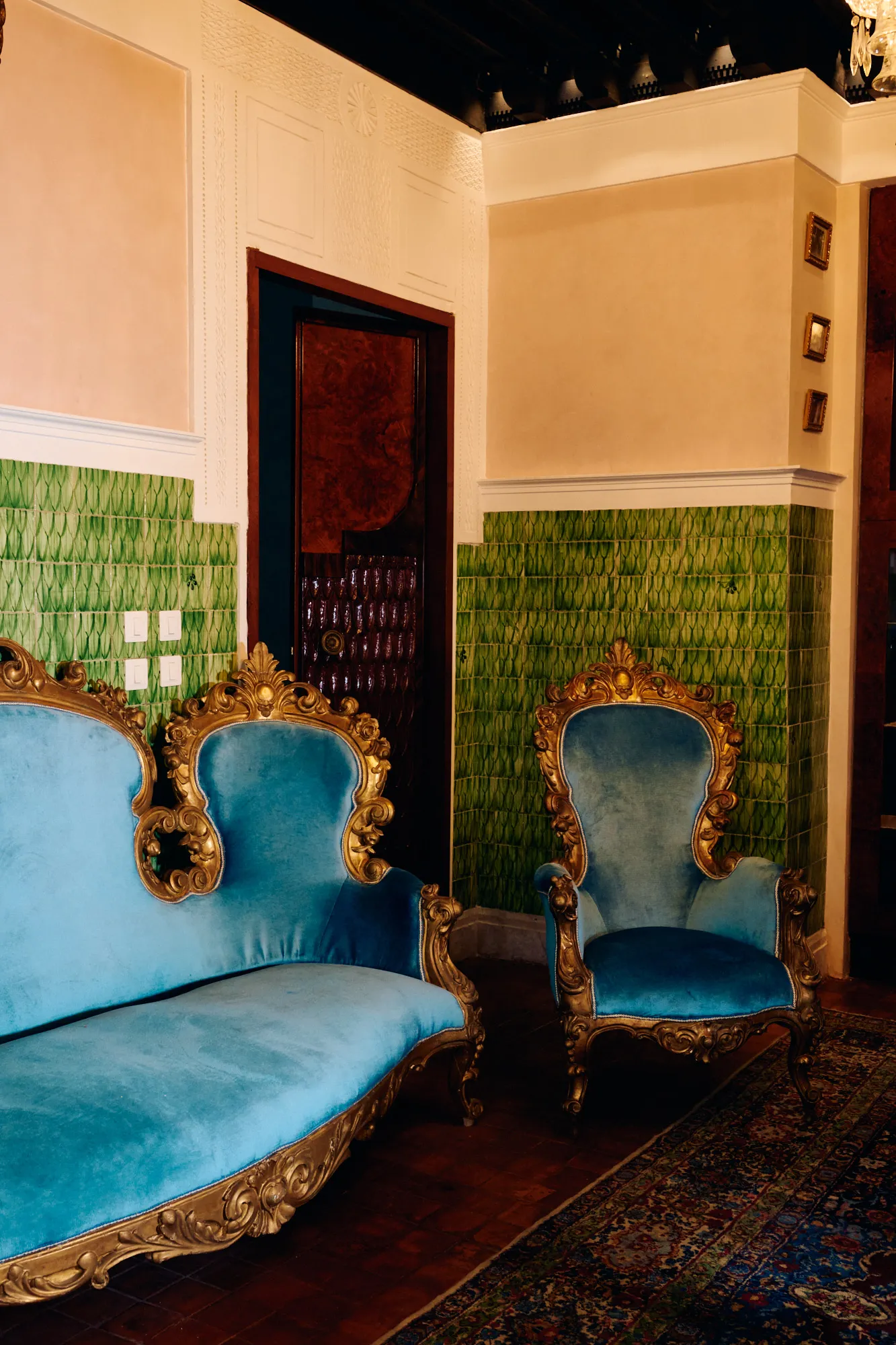 A salon with turquoise armchairs against green tilework.