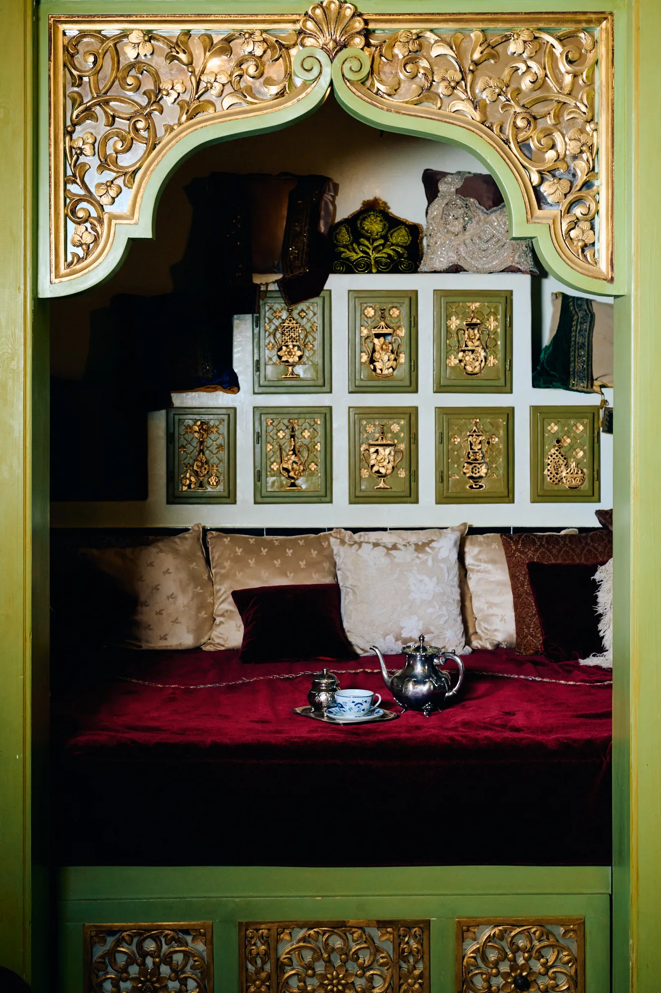 A carved green alcove framing a single bed dressed in red.