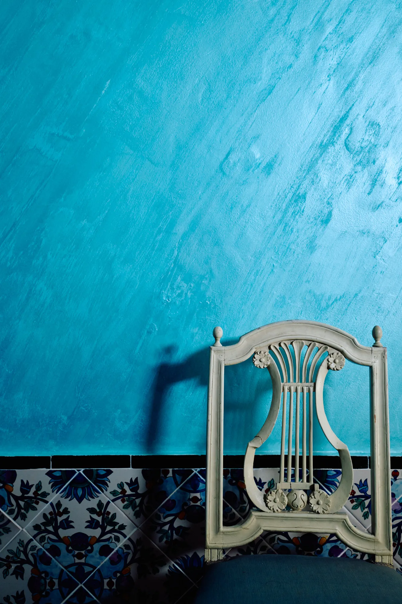 A white chair against turquoise plaster and blue tilework.