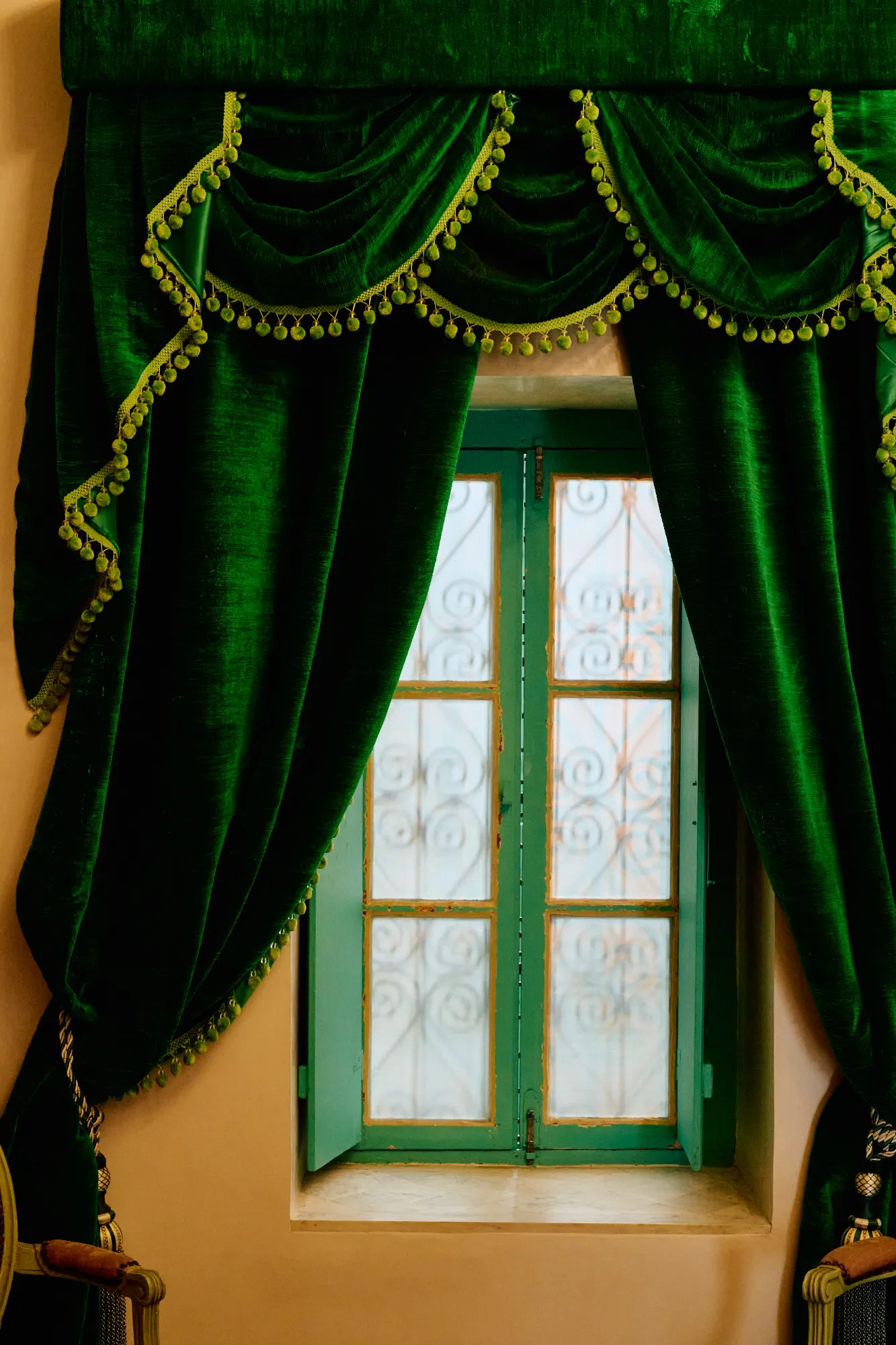 A green velvet curtain drawn back from a tall window.