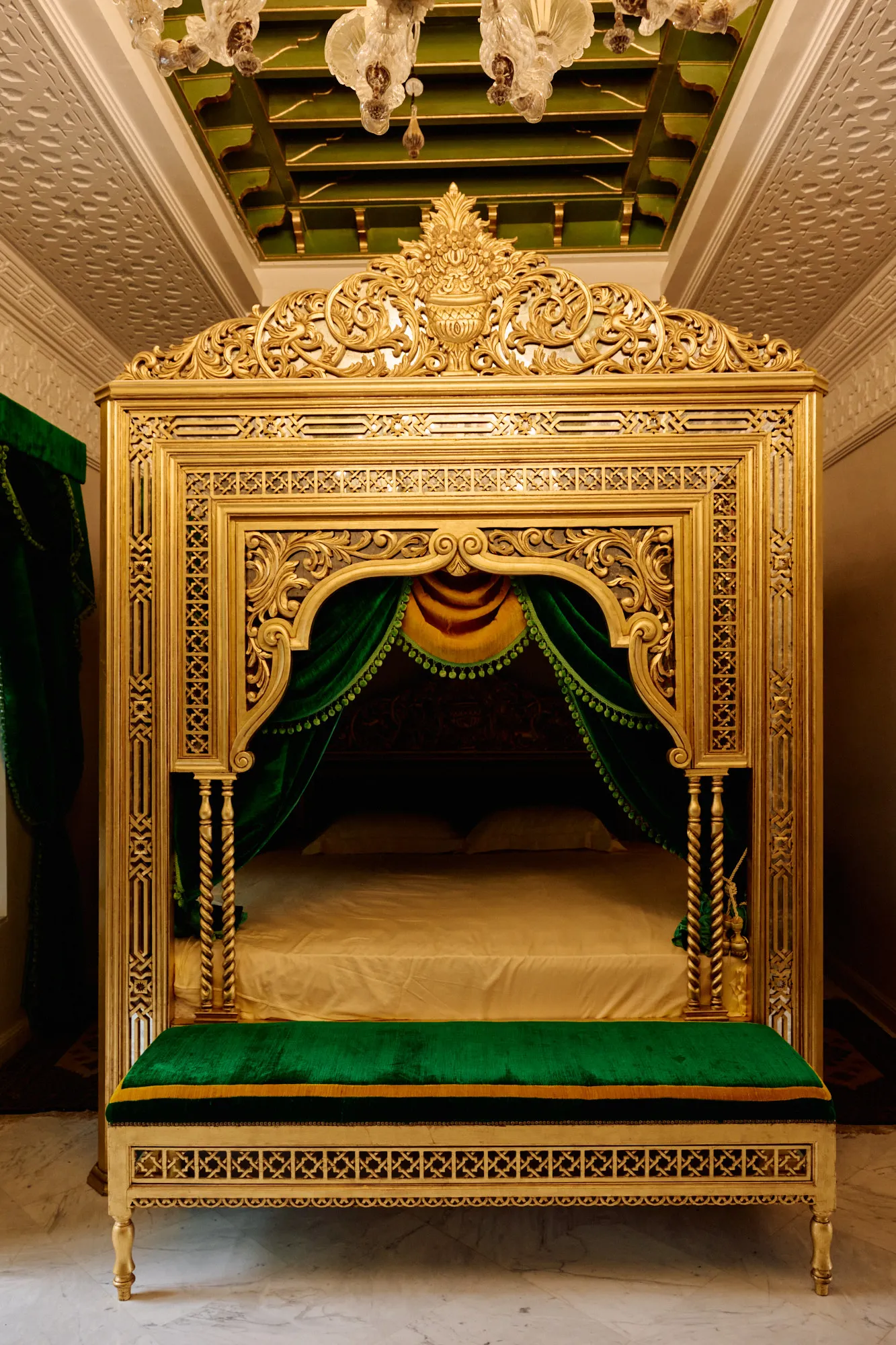 A gilded canopy bed hung with green velvet beneath a painted ceiling.