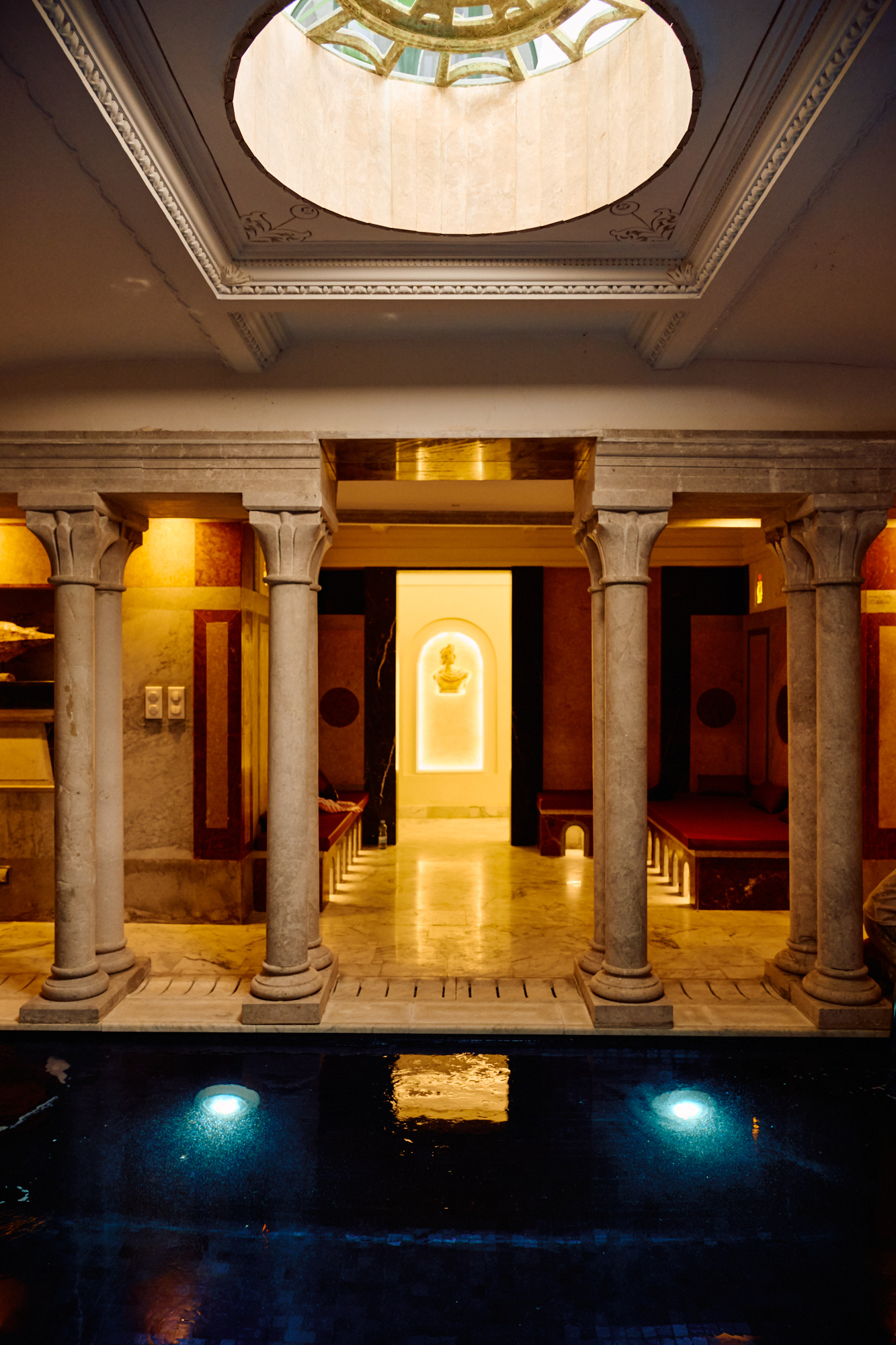 Une colonnade de marbre au-dessus de l'eau éclairée du bassin couvert.