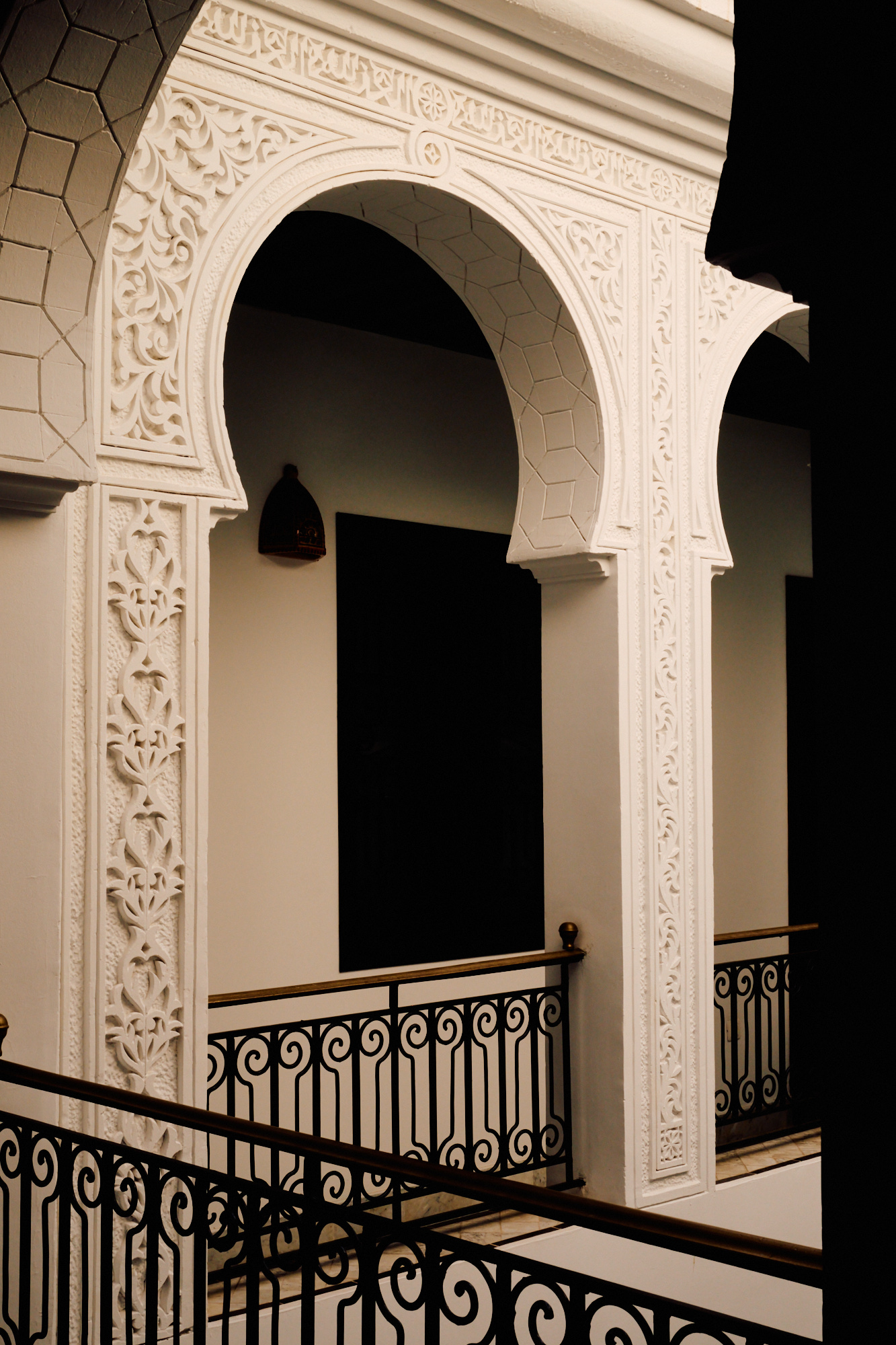 Des arches de plâtre blanc ouvrant sur la galerie, au-dessus d'une rambarde de fer.