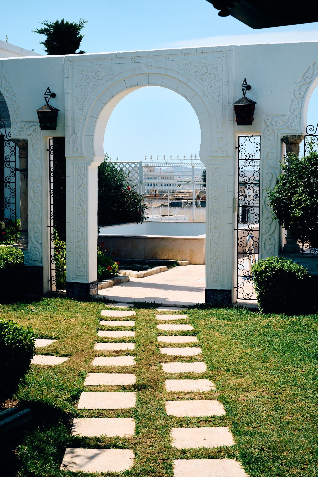 Une allée de dalles traversant le jardin vers une arche blanche.