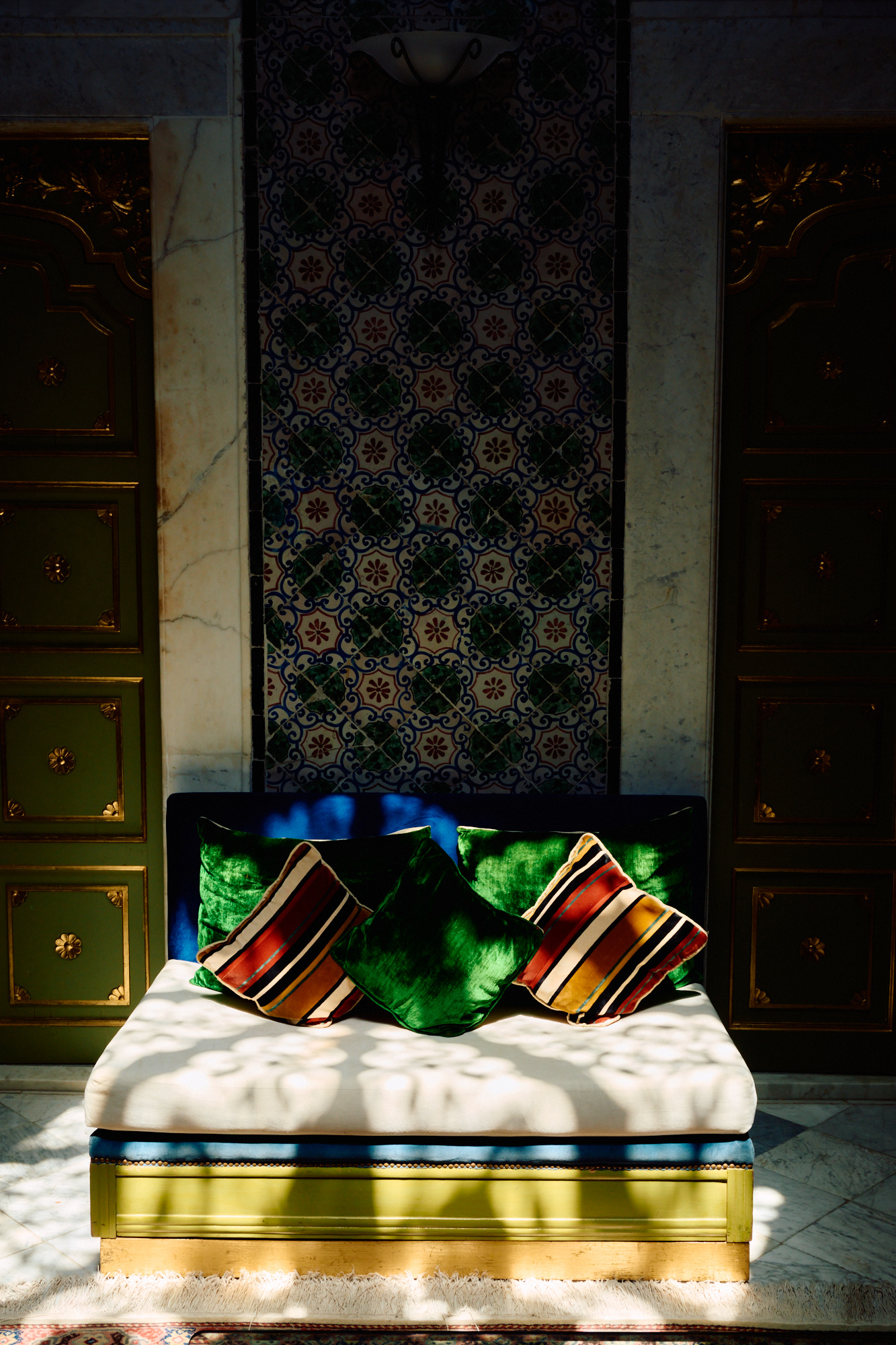 Une banquette au linge rayé et aux coussins verts, en plein soleil.