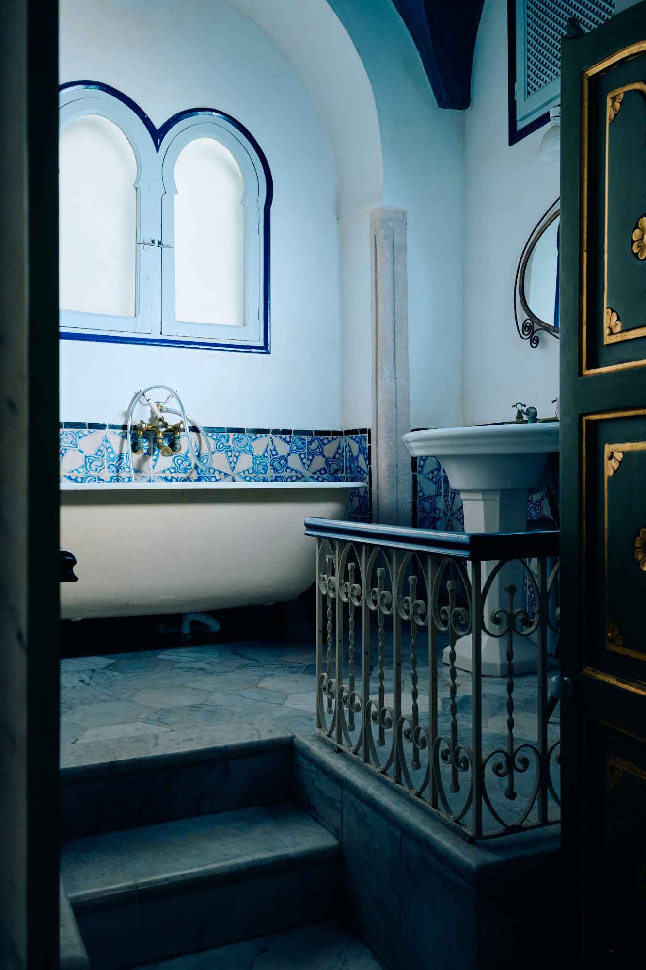 La salle de bain : une baignoire sur pieds contre la faïence bleue, sous une fenêtre en arc.