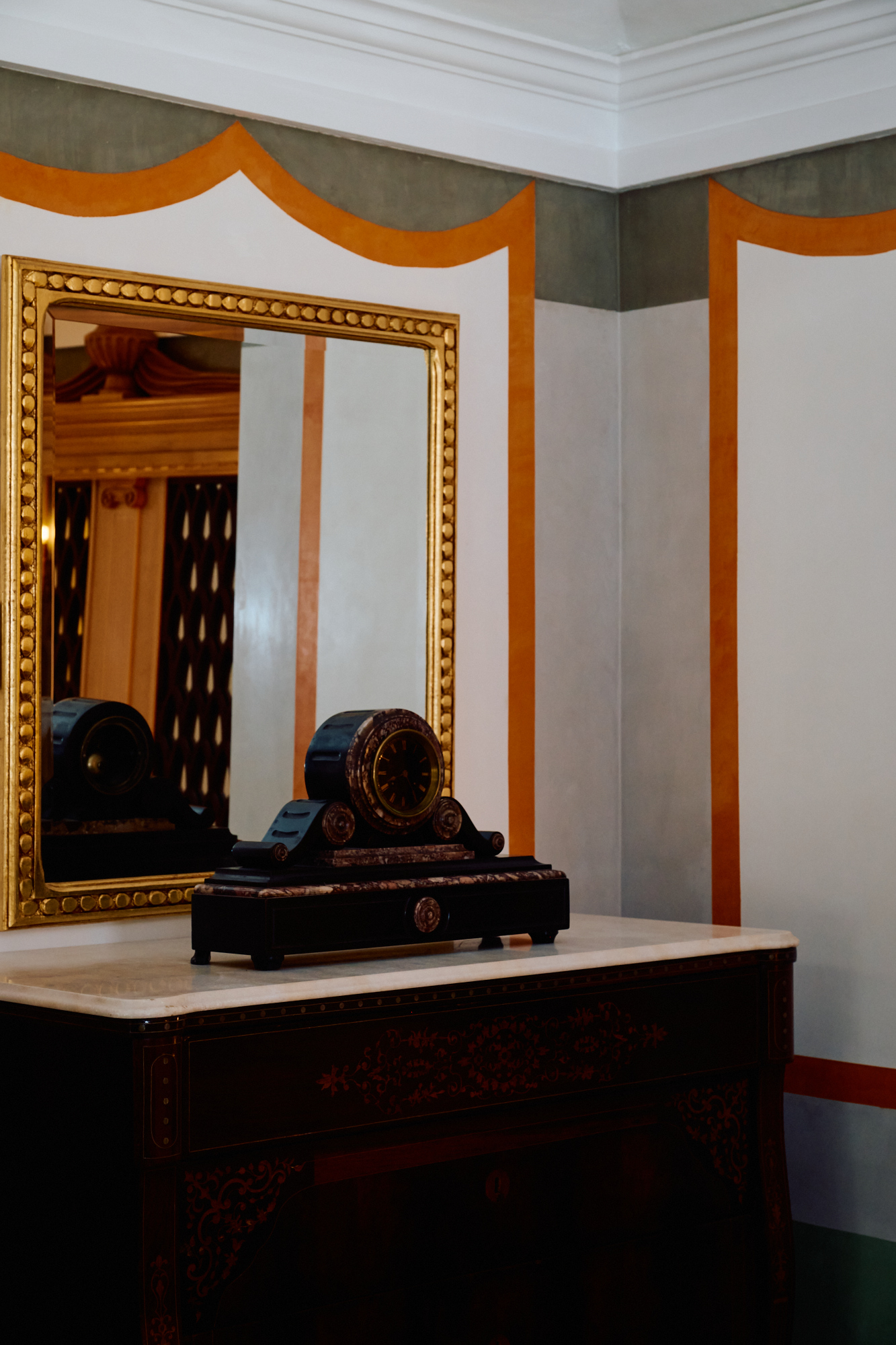 Un miroir doré au-dessus d'une console et d'un buste, sur des murs pâles filetés d'orange.