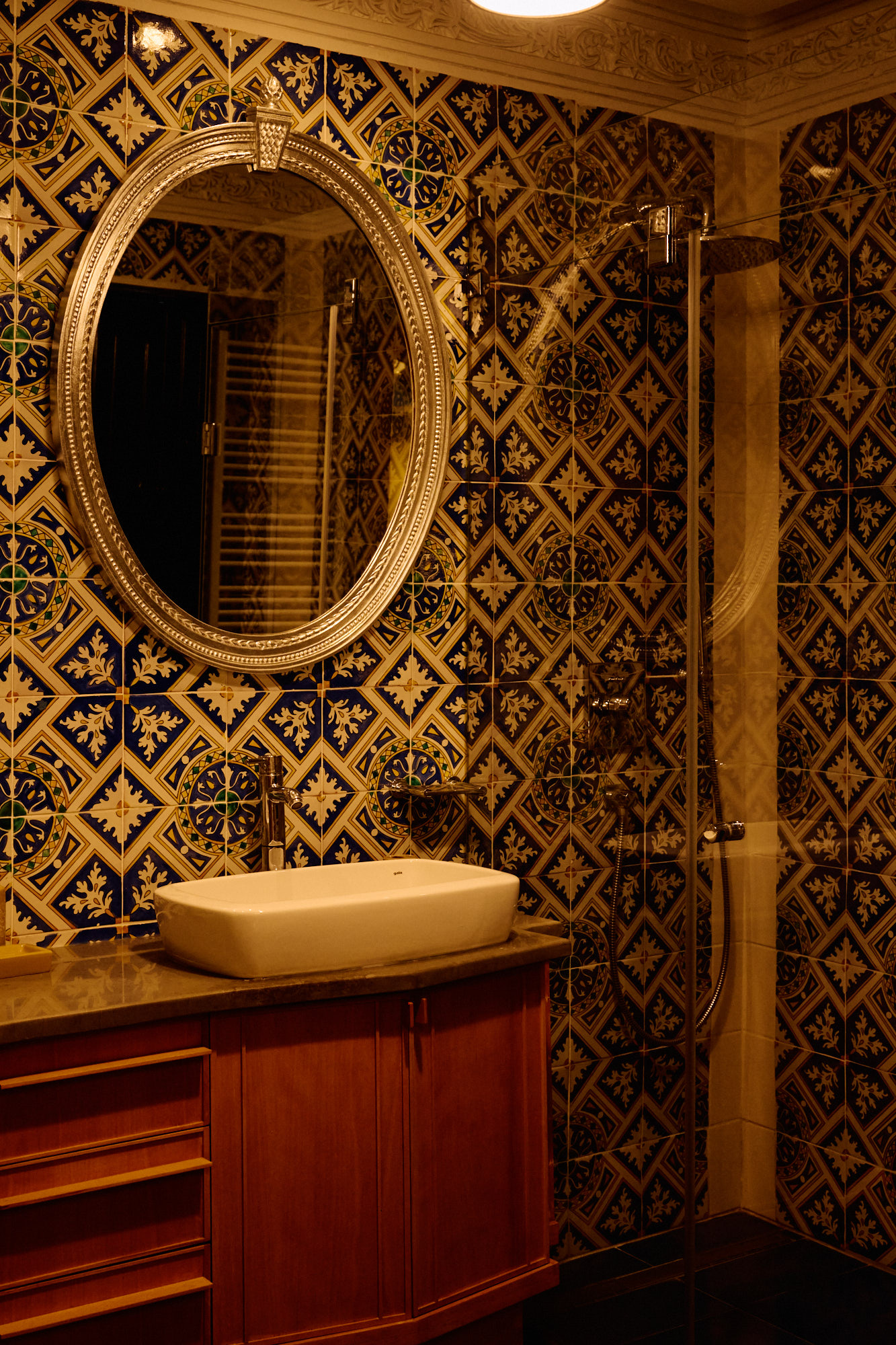 Un miroir ovale doré au-dessus d'un meuble de bois, sur une faïence bleue et or.